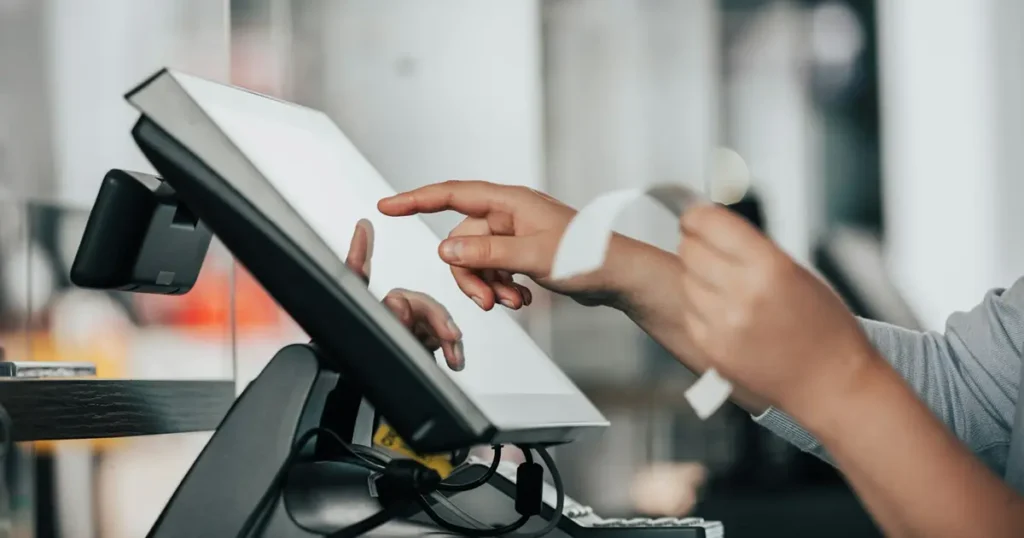 Close-up van de handen van een multistore verkoopster die een aanslag in de kassa doet.